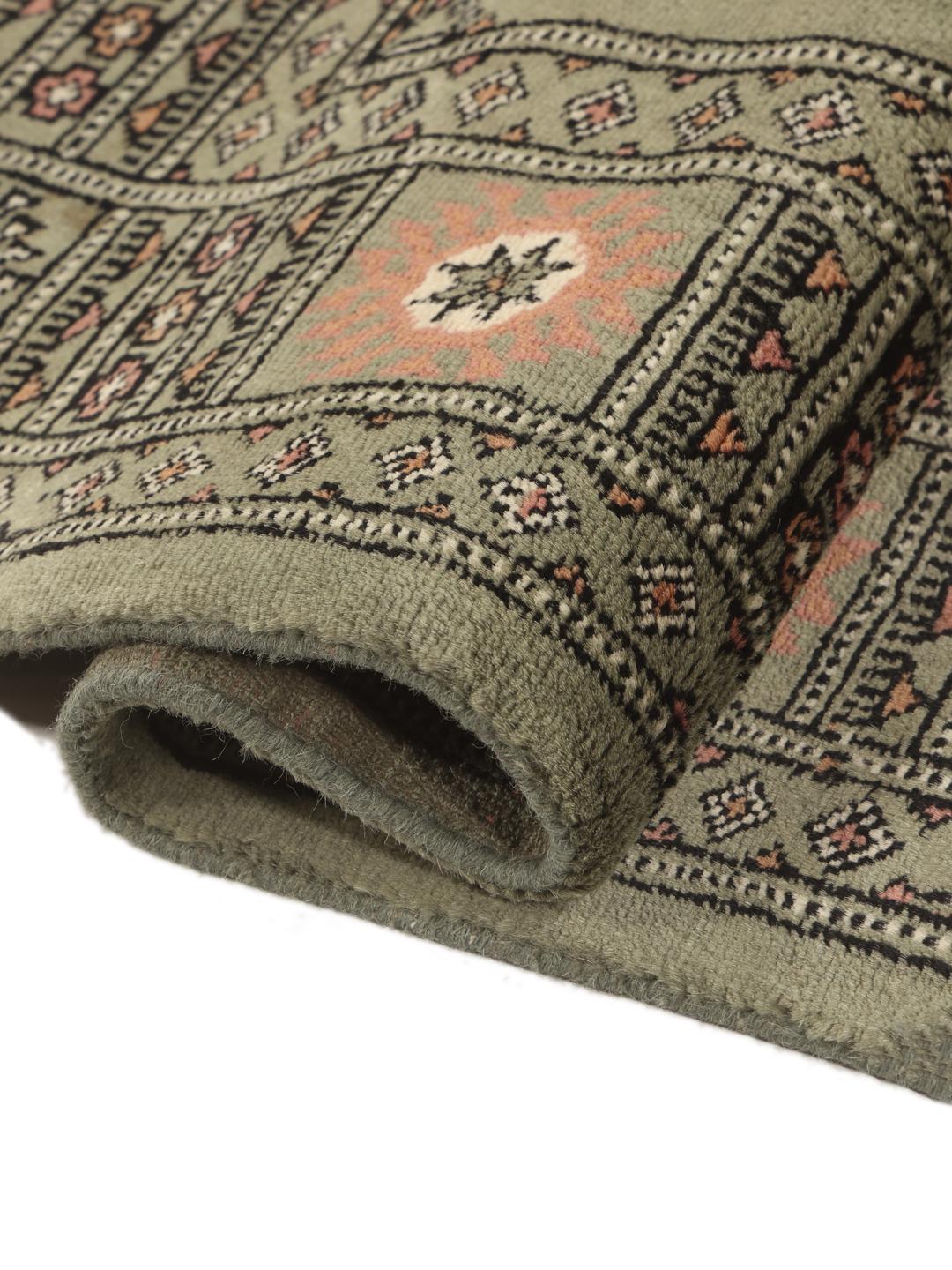 A hand-knotted green Pakistan Bokhara rug with traditional repeating motifs.
