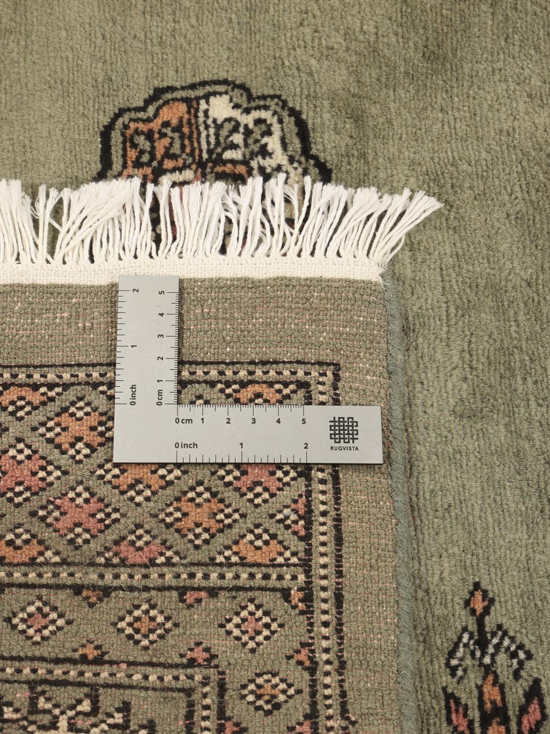 A hand-knotted green Pakistan Bokhara rug with traditional repeating motifs.