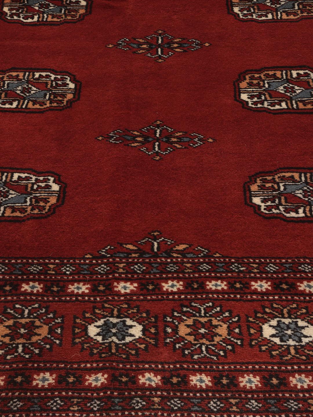 Un tapis Pakistan Bokhara noué à la main avec un champ rouge profond et des motifs géométriques répétitifs.