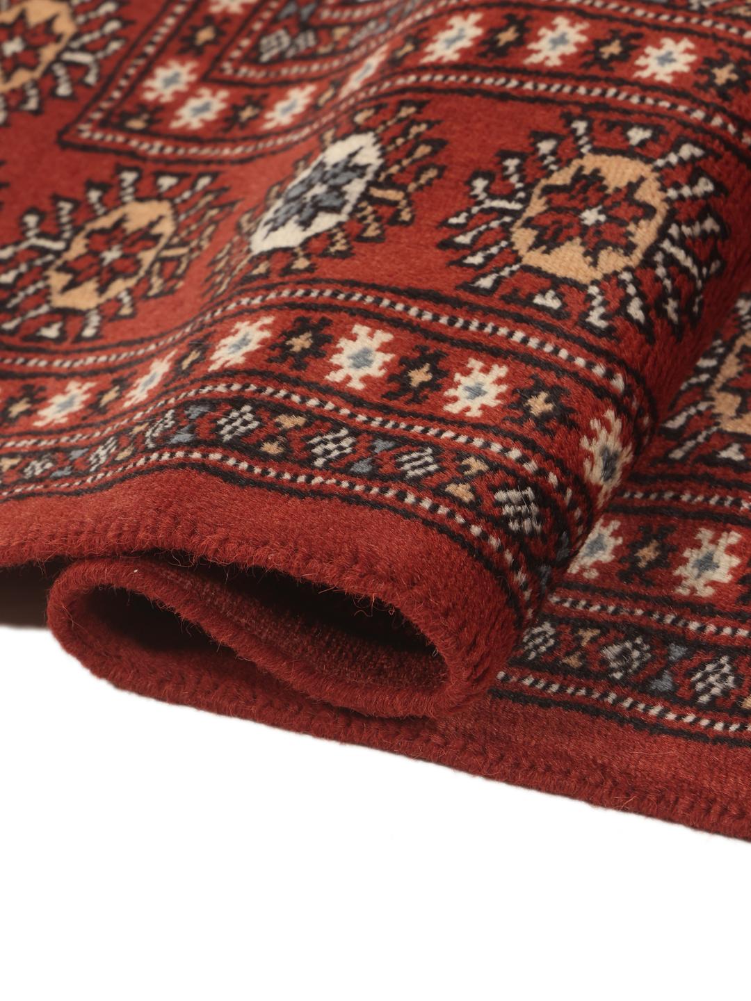 Un tapis Pakistan Bokhara noué à la main avec un champ rouge profond et des motifs géométriques répétitifs.