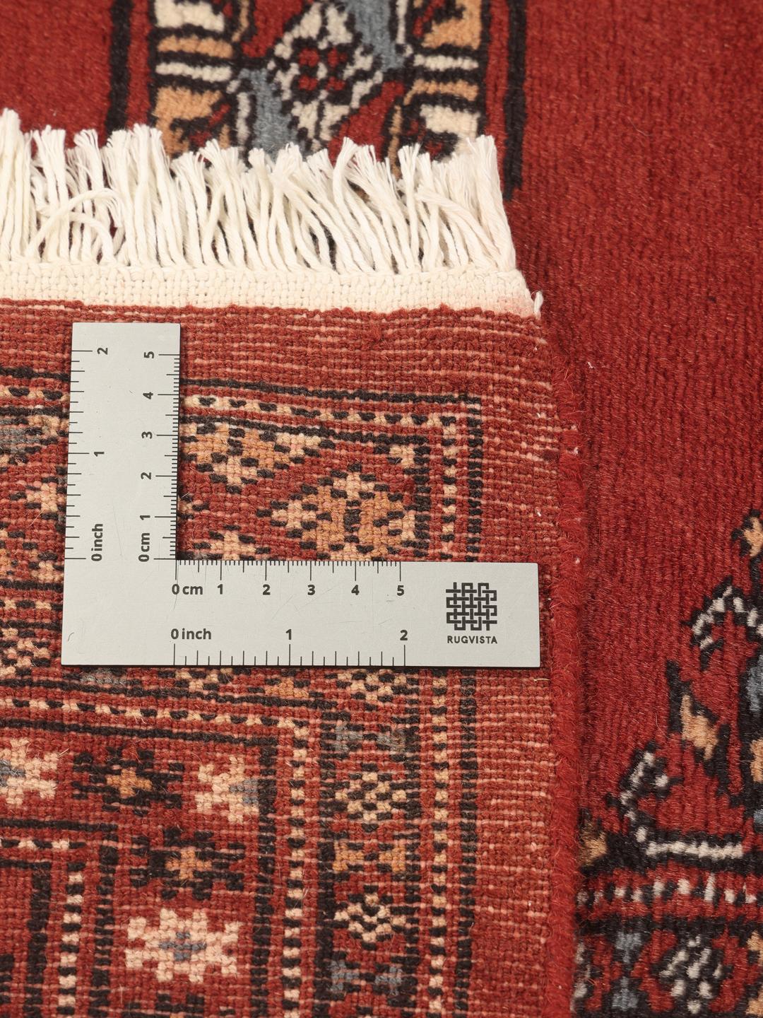 Un tapis Pakistan Bokhara noué à la main avec un champ rouge profond et des motifs géométriques répétitifs.