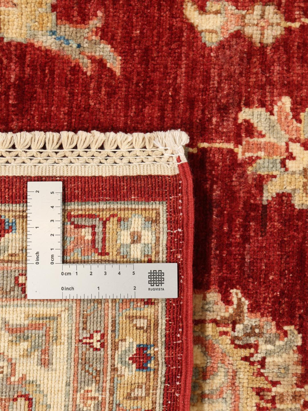 Un covor înnodat manual din Pakistan cu câmp roșu și motive florale într-o bordură decorativă.
