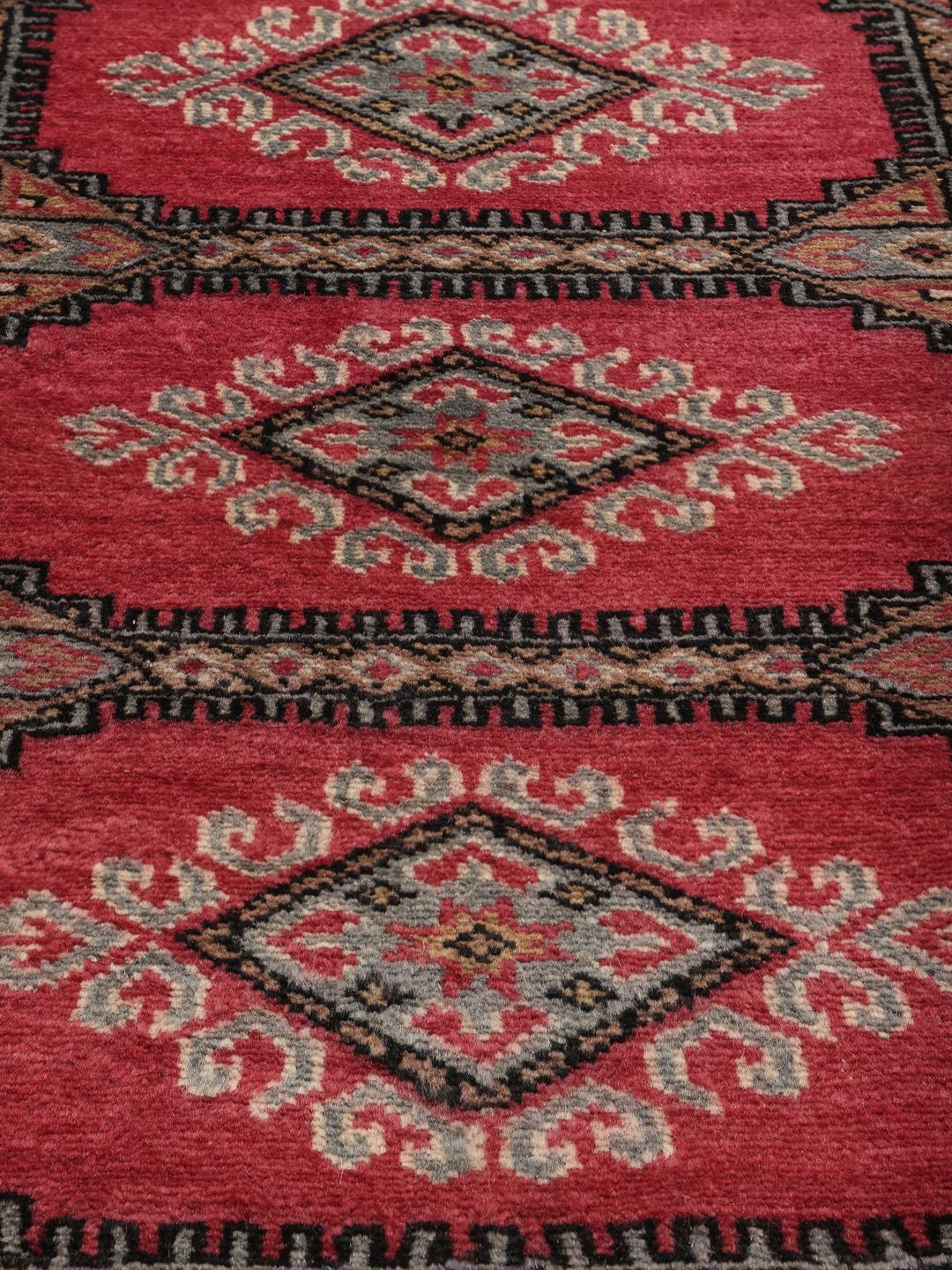 A small, rectangular Pakistan Bokhara 2ply rug in dark-red with geometric medallions.