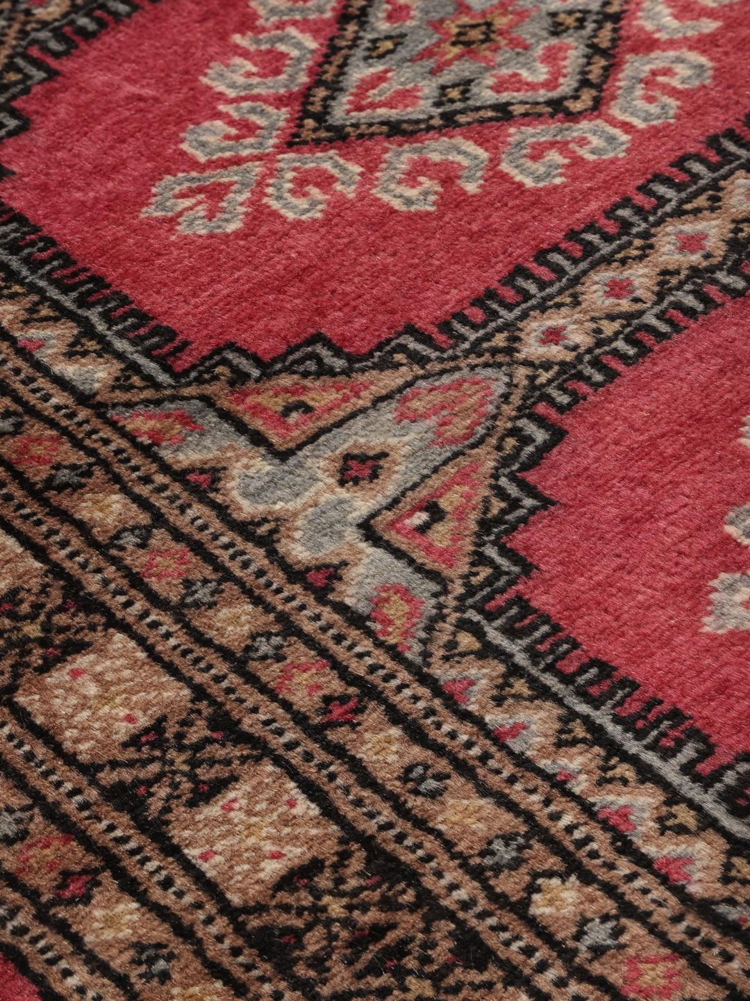 A small, rectangular Pakistan Bokhara 2ply rug in dark-red with geometric medallions.