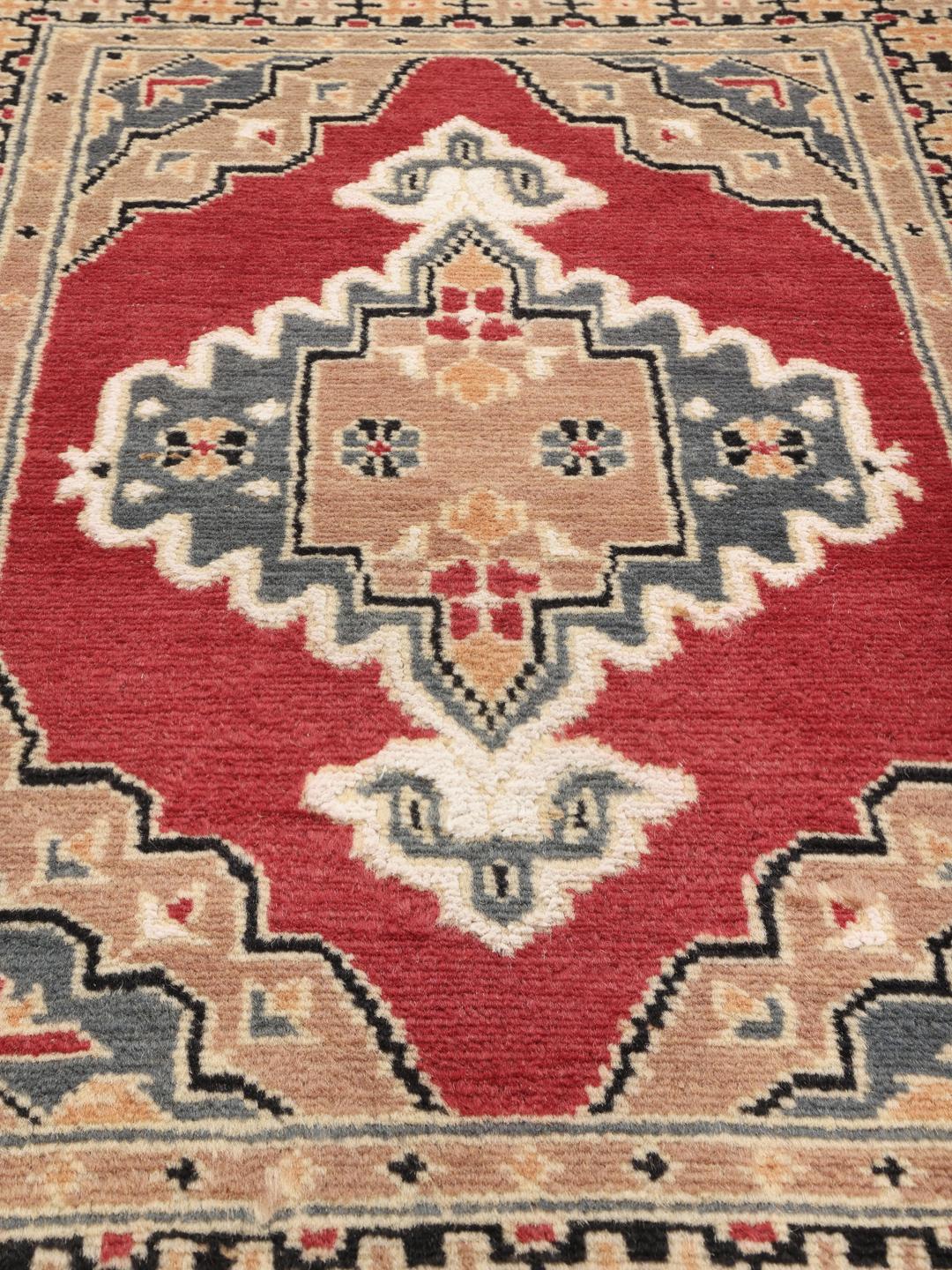 A hand-knotted Pakistan Bokhara wool rug featuring a red and beige geometric design.