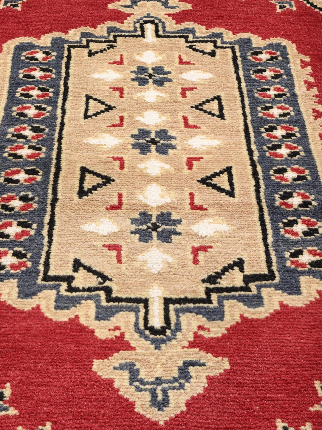 A hand-knotted Pakistan Bokhara rug with a red field and geometric medallion in a home setting.