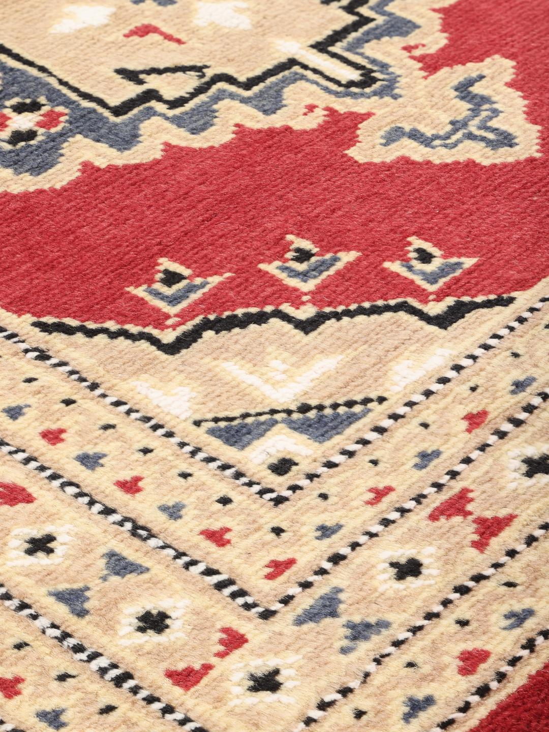 A hand-knotted Pakistan Bokhara rug with a red field and geometric medallion in a home setting.