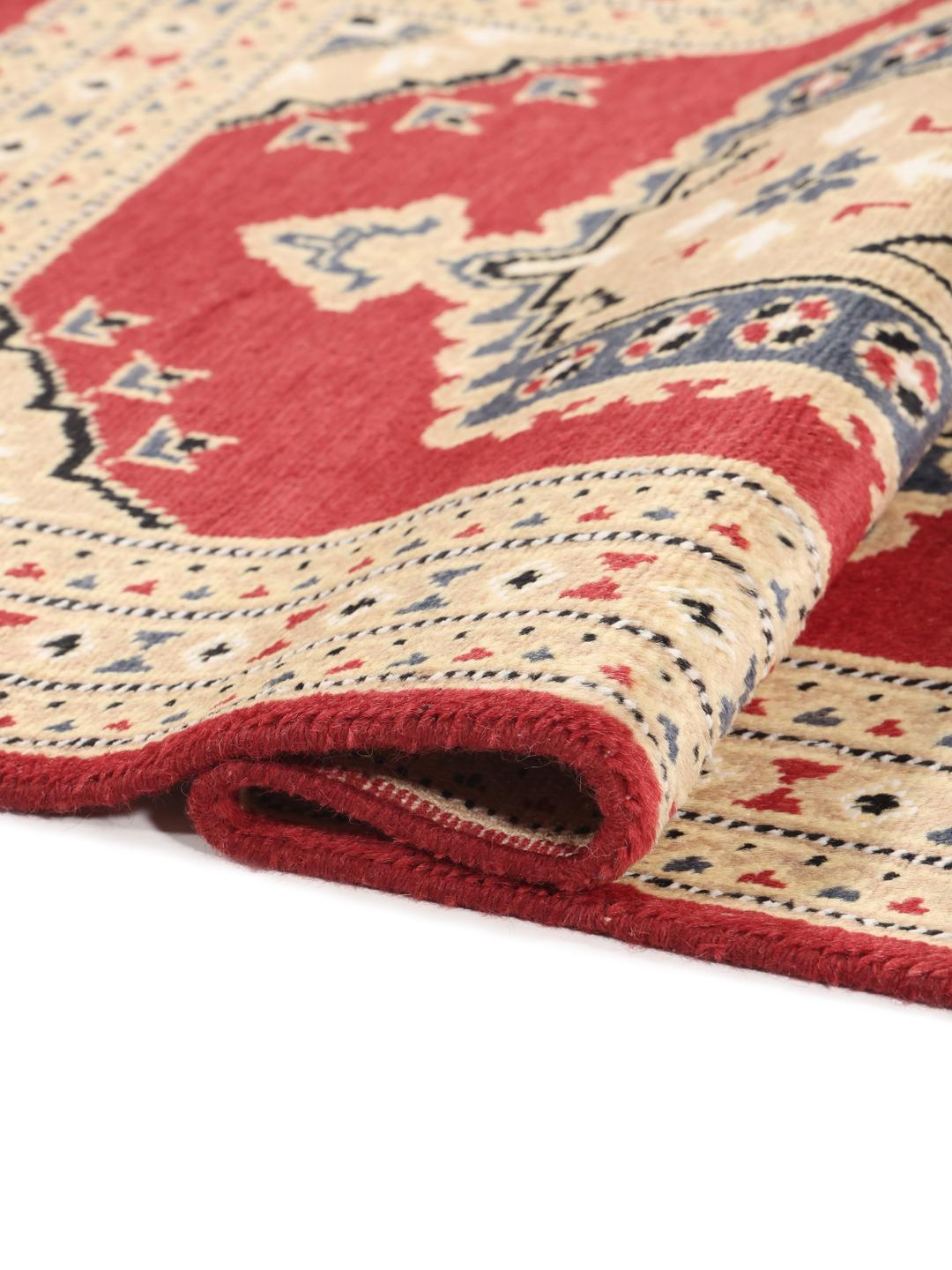 A hand-knotted Pakistan Bokhara rug with a red field and geometric medallion in a home setting.