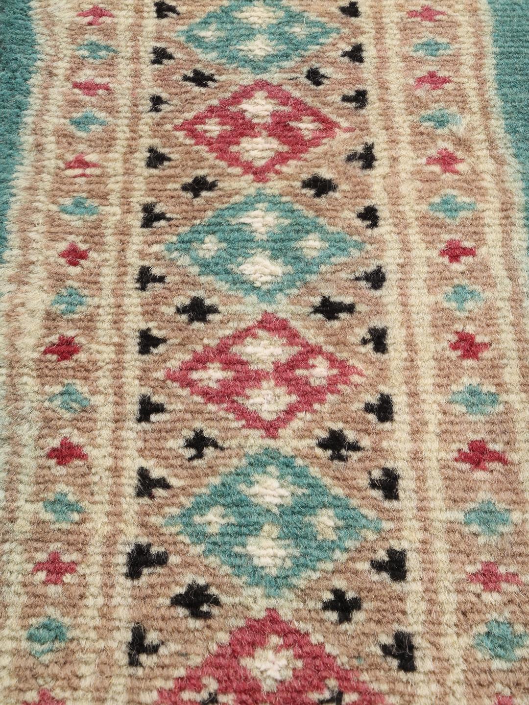 A hand-knotted Pakistan Bokhara 2ply rug with a teal border and geometric medallion pattern
