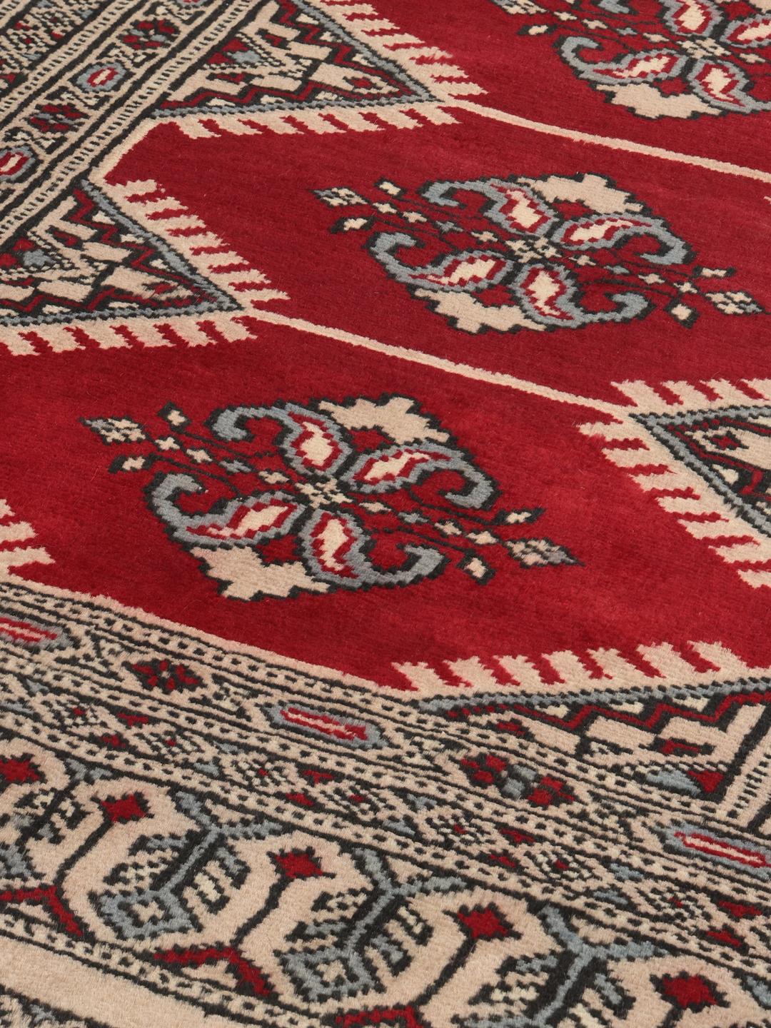 A hand-knotted Pakistan Bokhara rug with a deep red field and intricate geometric medallions.