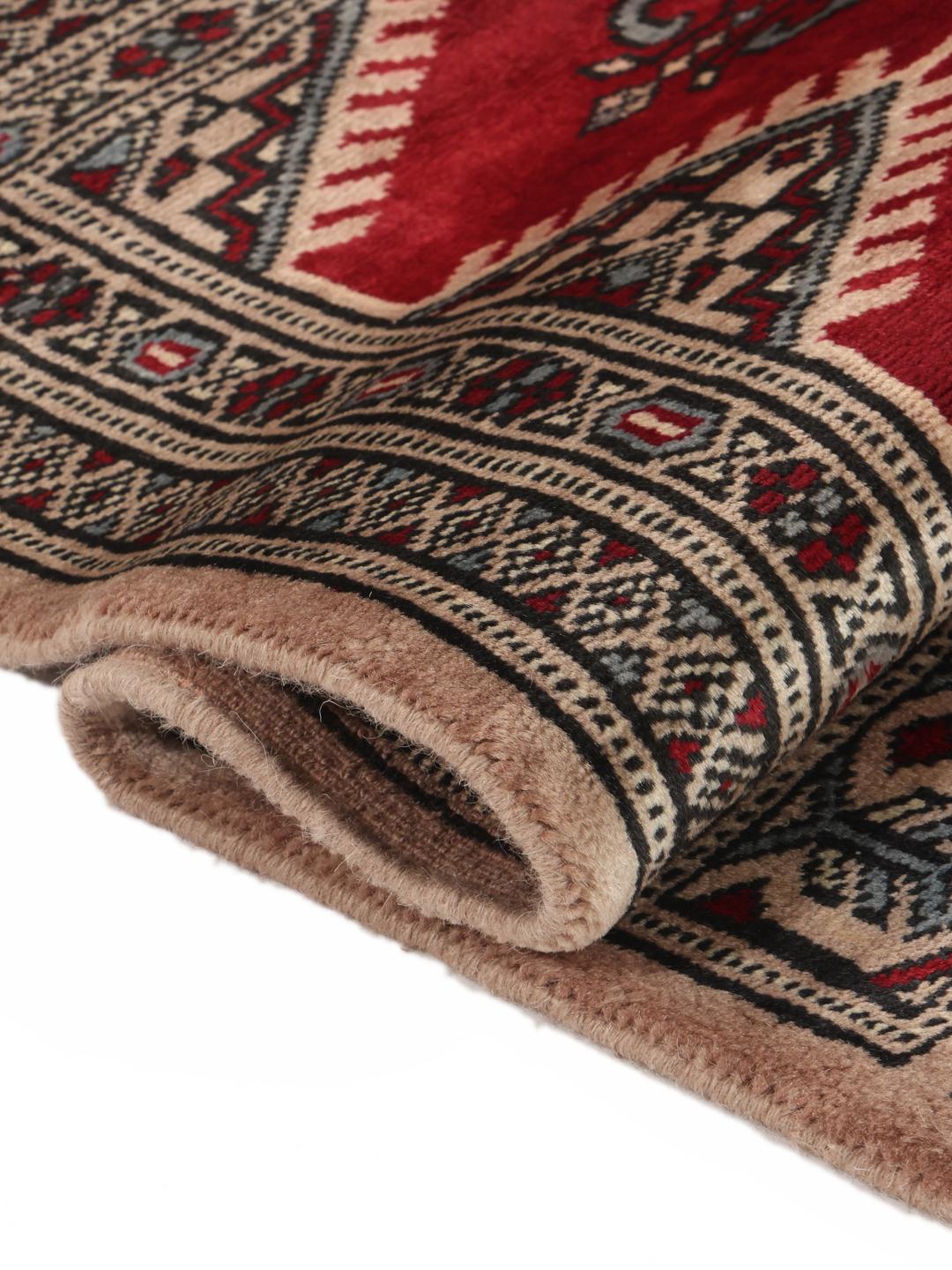 A hand-knotted Pakistan Bokhara rug with a deep red field and intricate geometric medallions.