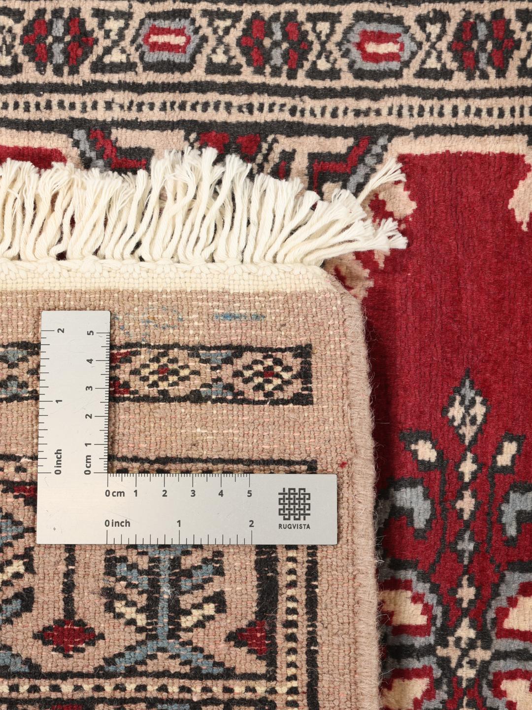 A hand-knotted Pakistan Bokhara rug with a deep red field and intricate geometric medallions.