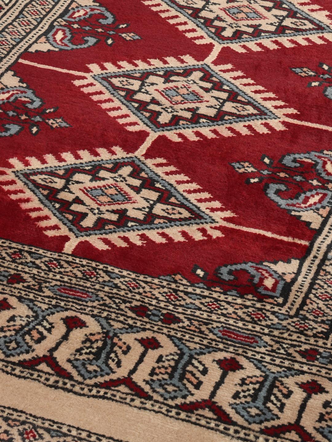 A hand-knotted Pakistan Bokhara rug in red and beige tones with traditional geometric motifs.