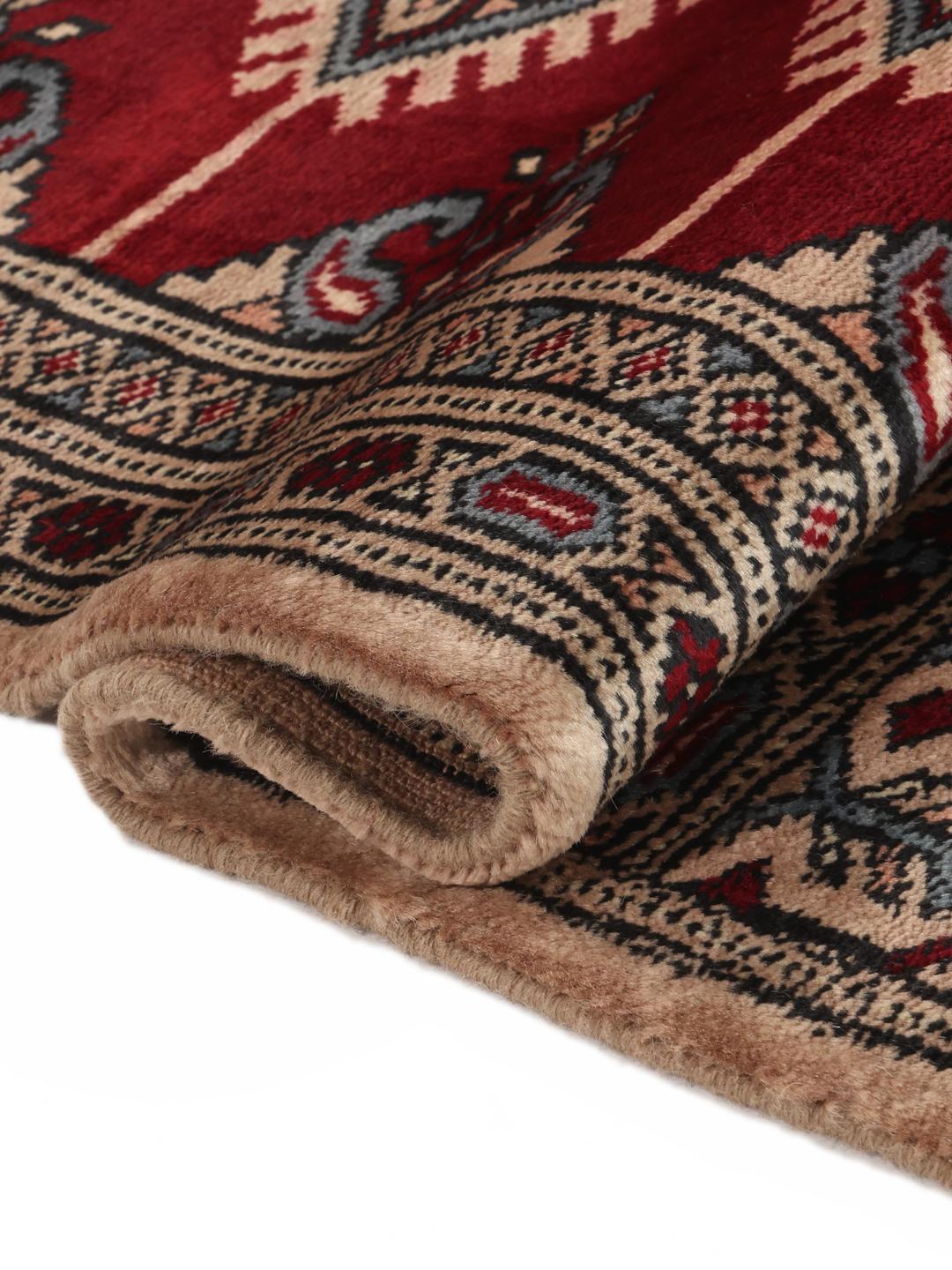 A hand-knotted Pakistan Bokhara rug in red and beige tones with traditional geometric motifs.