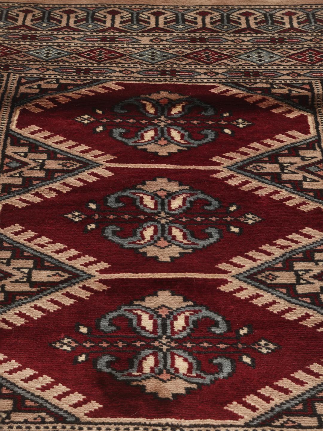 Een handgeknoopt Pakistan Bokhara tapijt met een rood veld en ingewikkelde geometrische en bloemrijke patronen.