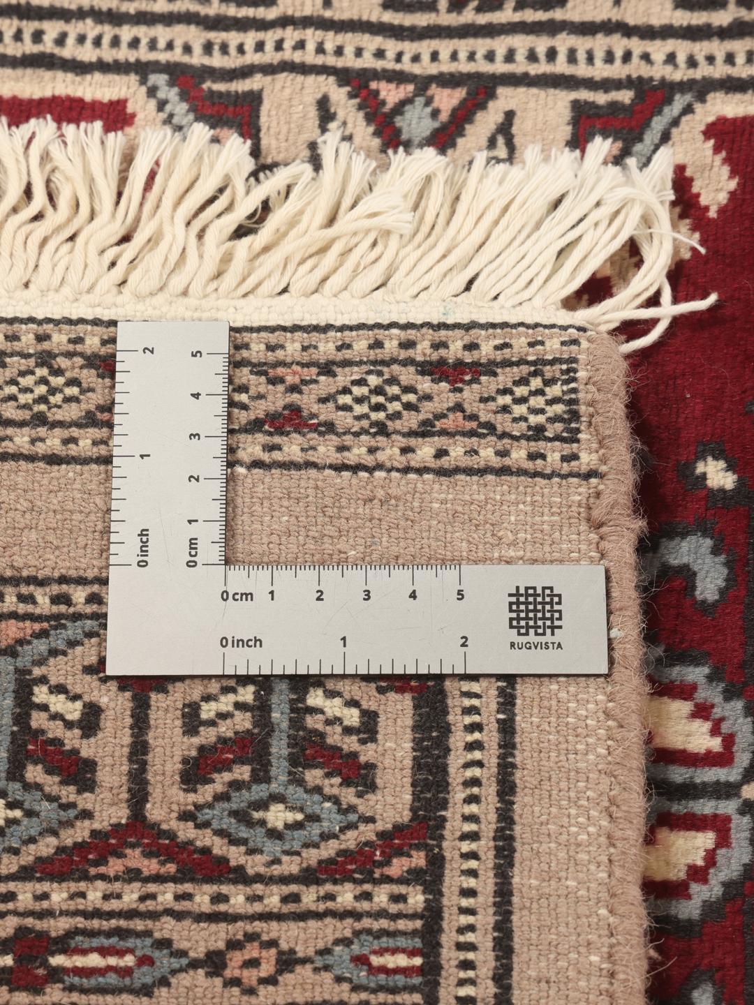Een handgeknoopt Pakistan Bokhara tapijt met een rood veld en ingewikkelde geometrische en bloemrijke patronen.