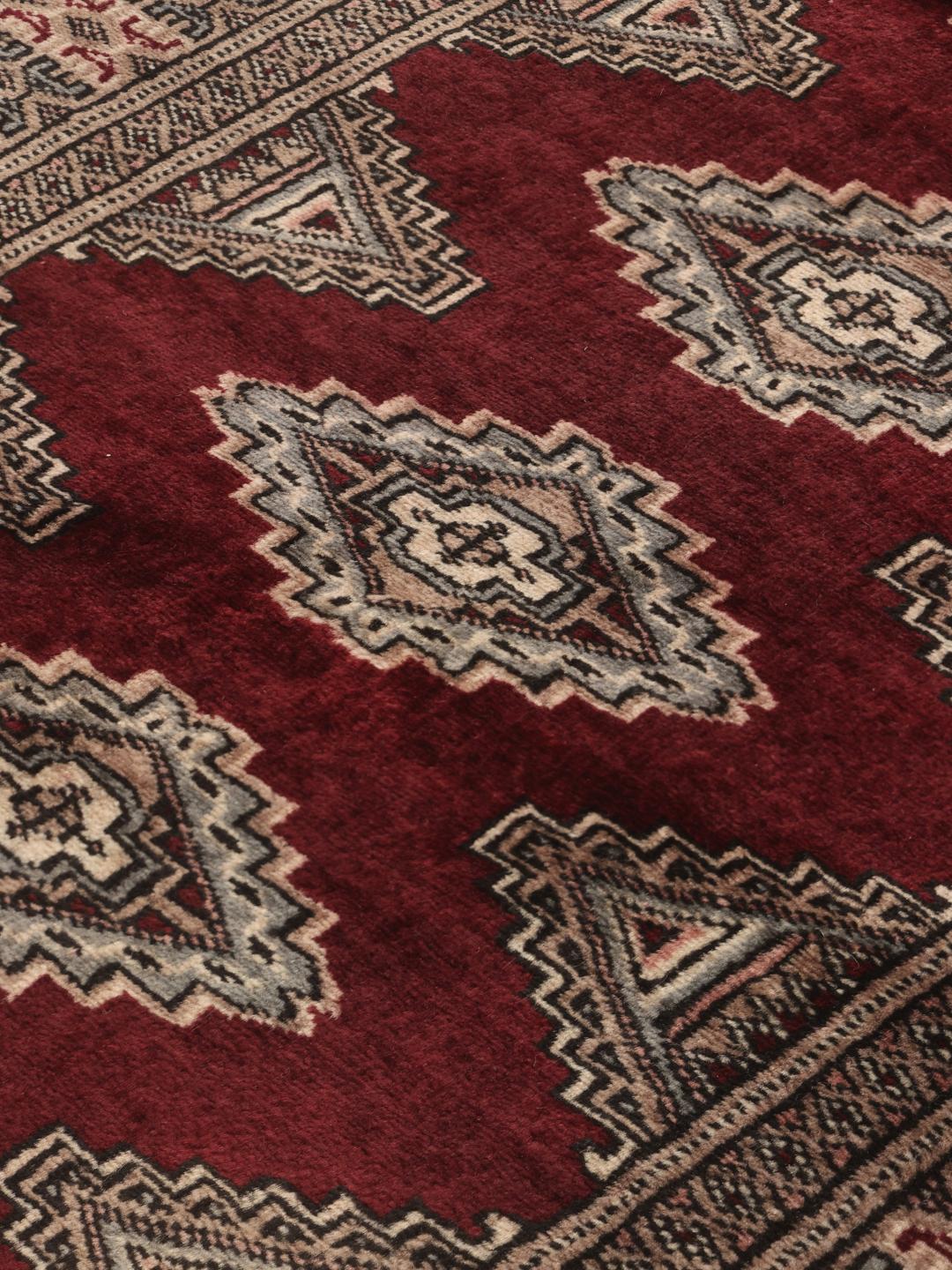 A hand-knotted Pakistan Bokhara rug featuring geometric medallions in dark-red and beige.