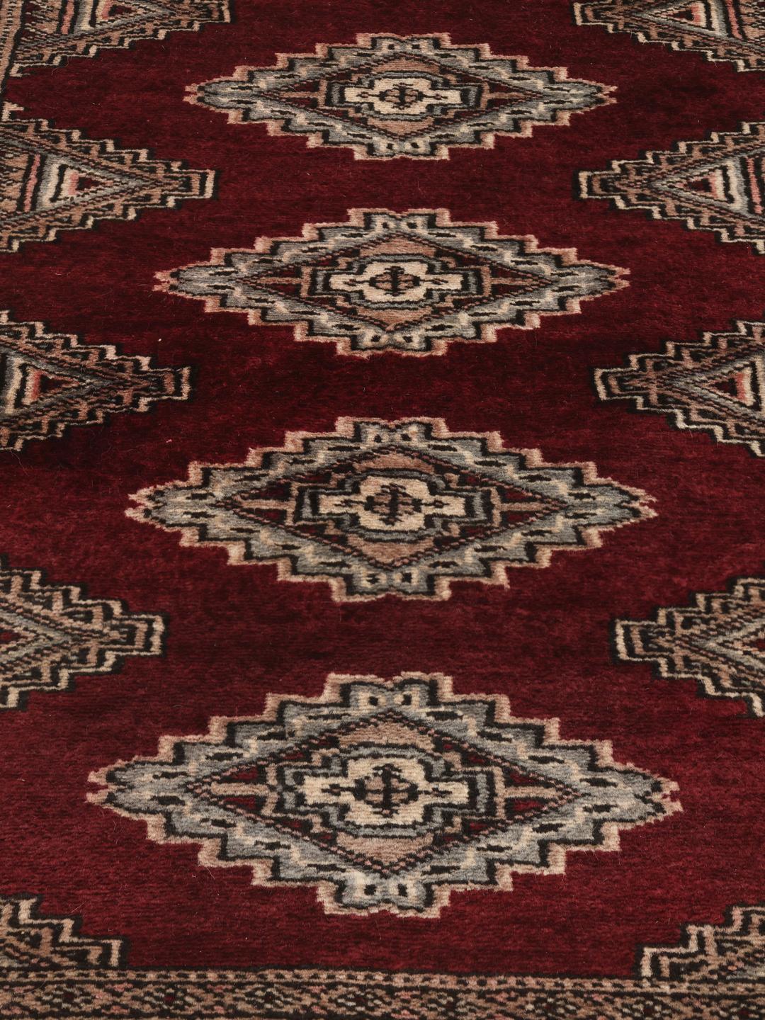 A hand-knotted Pakistan Bokhara rug featuring geometric medallions in dark-red and beige.