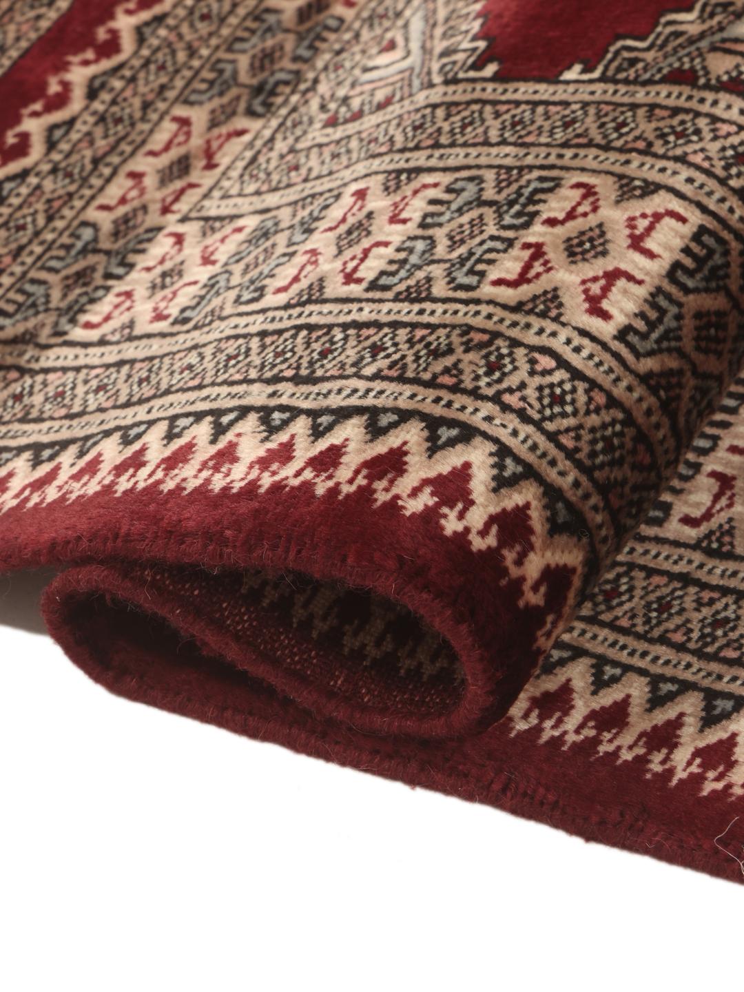 A hand-knotted Pakistan Bokhara rug featuring geometric medallions in dark-red and beige.