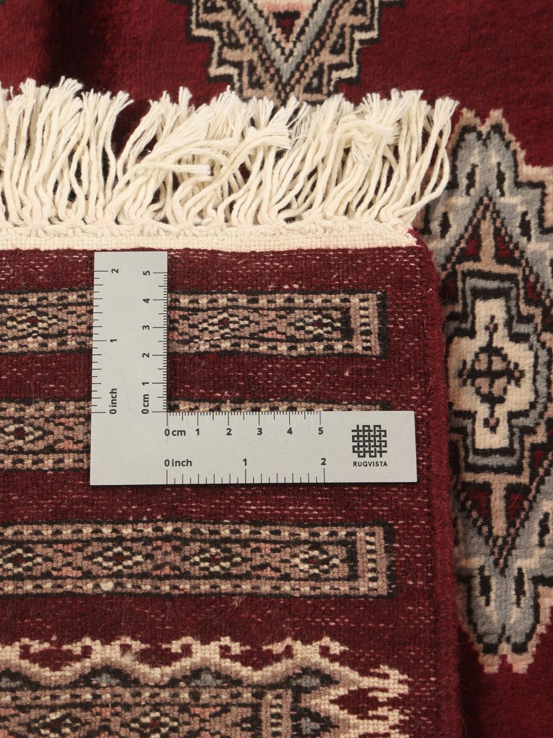 A hand-knotted Pakistan Bokhara rug featuring geometric medallions in dark-red and beige.