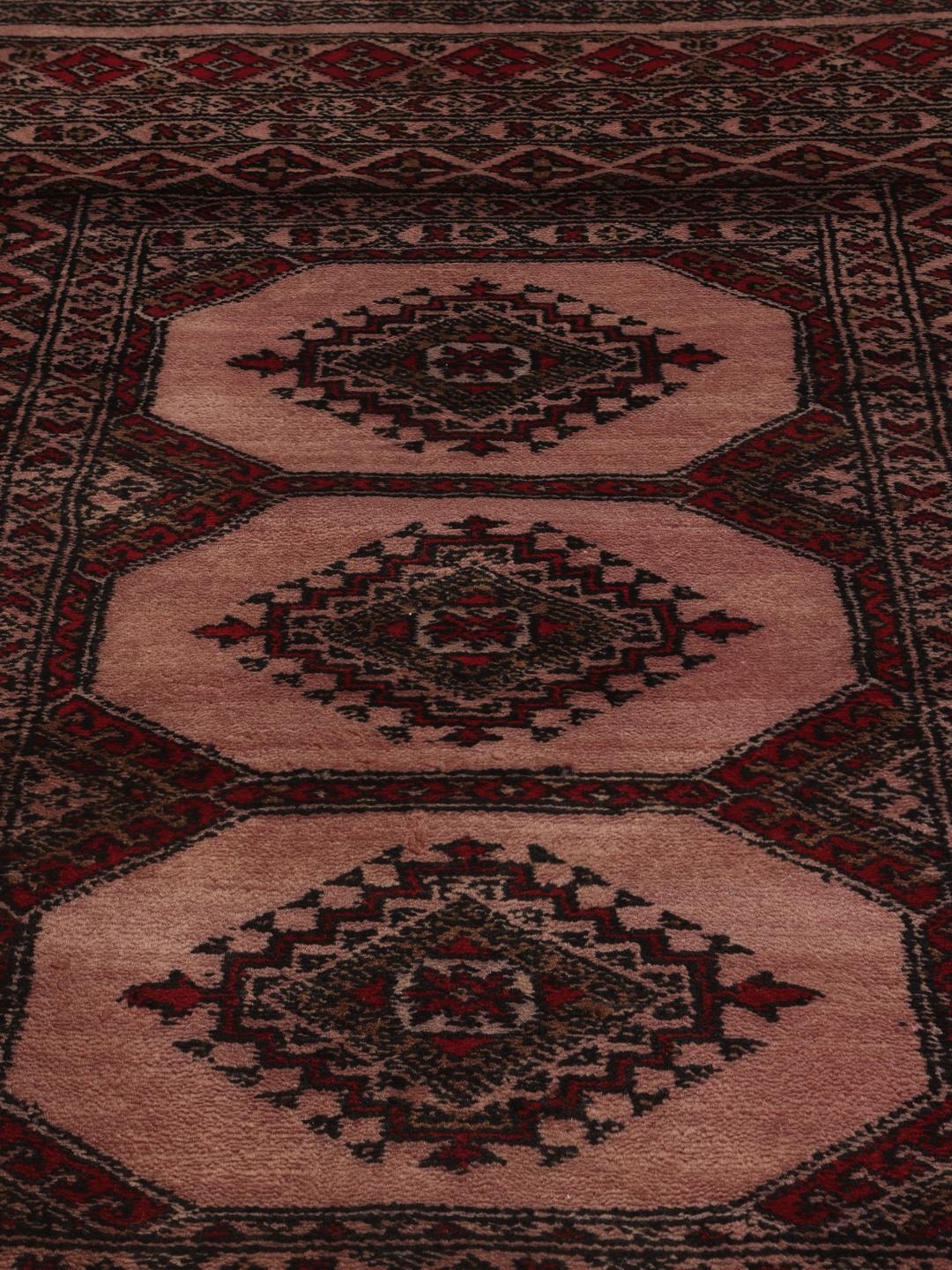 Een rechthoekig handgemaakt Pakistan Bokhara 3ply tapijt in roze met geometrische medaillonpatronen.