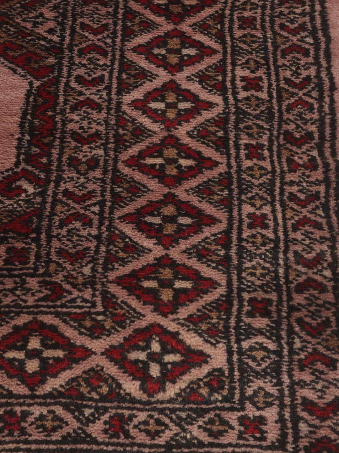 Een rechthoekig handgemaakt Pakistan Bokhara 3ply tapijt in roze met geometrische medaillonpatronen.