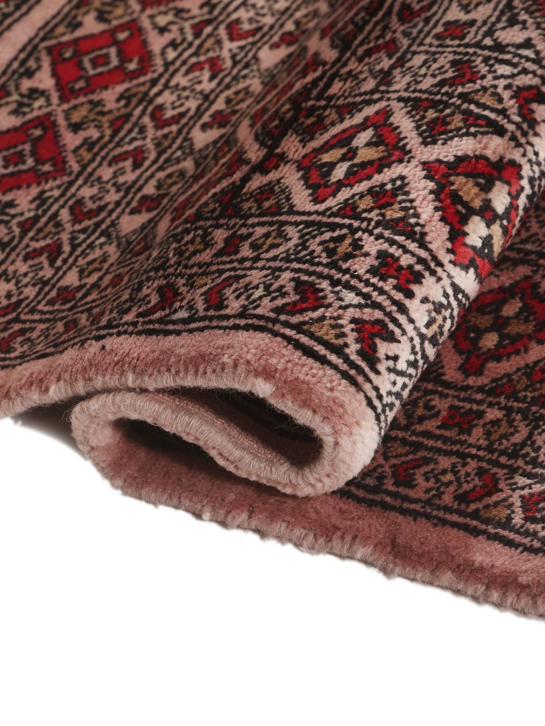 Een rechthoekig handgemaakt Pakistan Bokhara 3ply tapijt in roze met geometrische medaillonpatronen.
