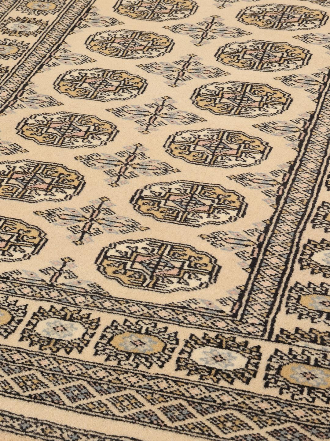 A hand-knotted Pakistan Bokhara rug with a beige field and traditional geometric motifs.