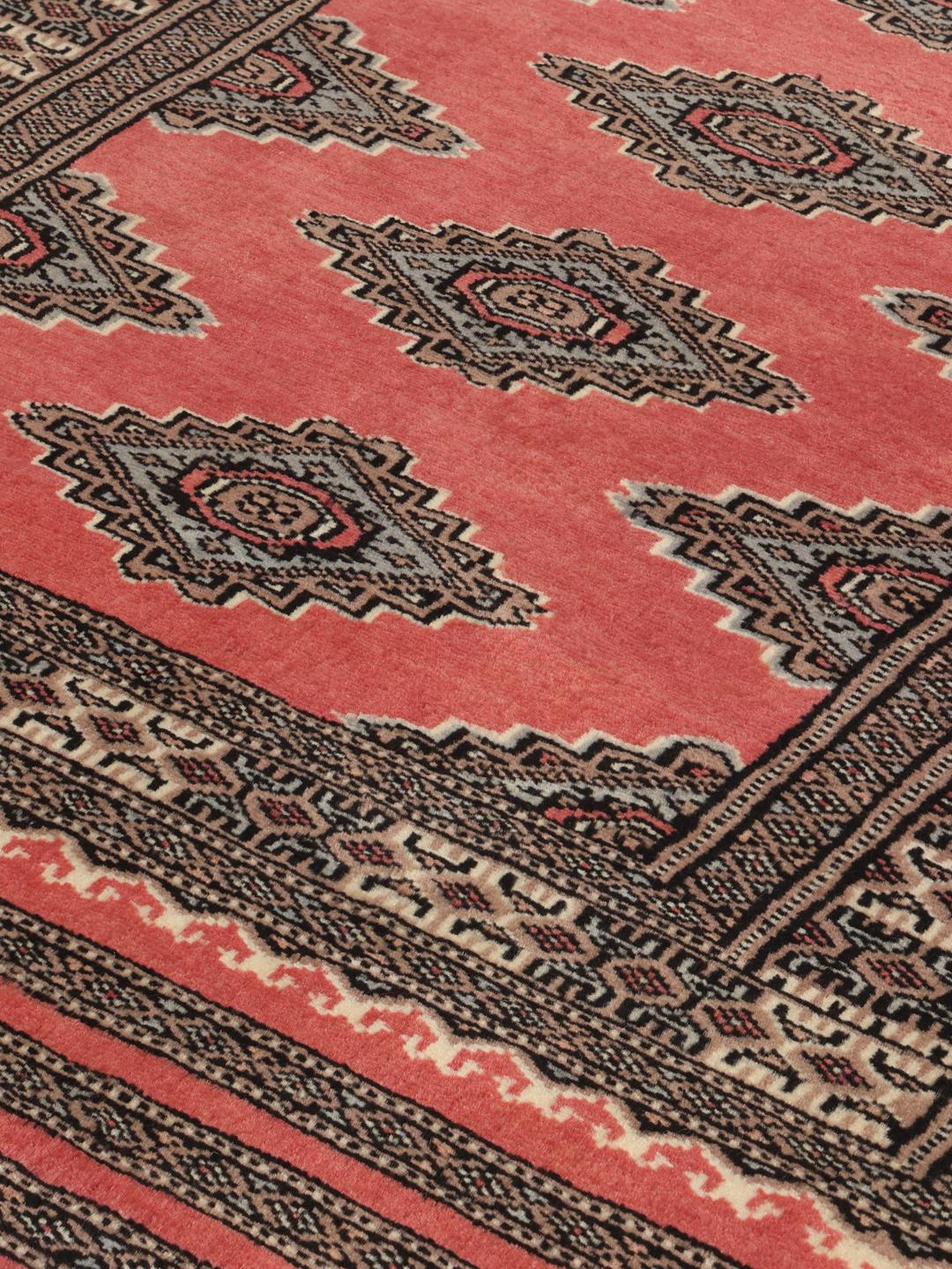 A hand-knotted red Pakistan Bokhara rug with traditional geometric motifs.