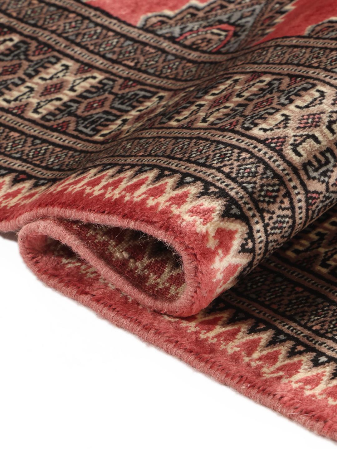A hand-knotted red Pakistan Bokhara rug with traditional geometric motifs.