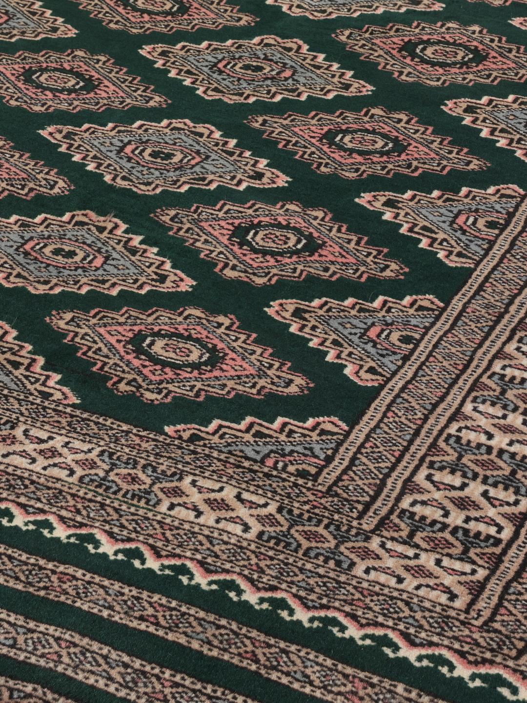 A hand-knotted Pakistan Bokhara rug with a dark green field and geometric patterns.