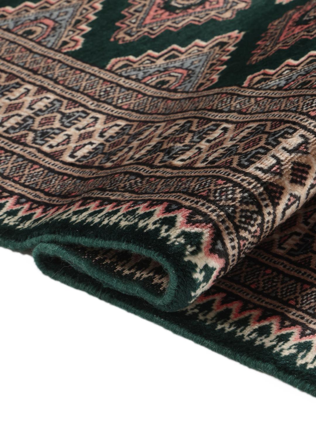 A hand-knotted Pakistan Bokhara rug with a dark green field and geometric patterns.