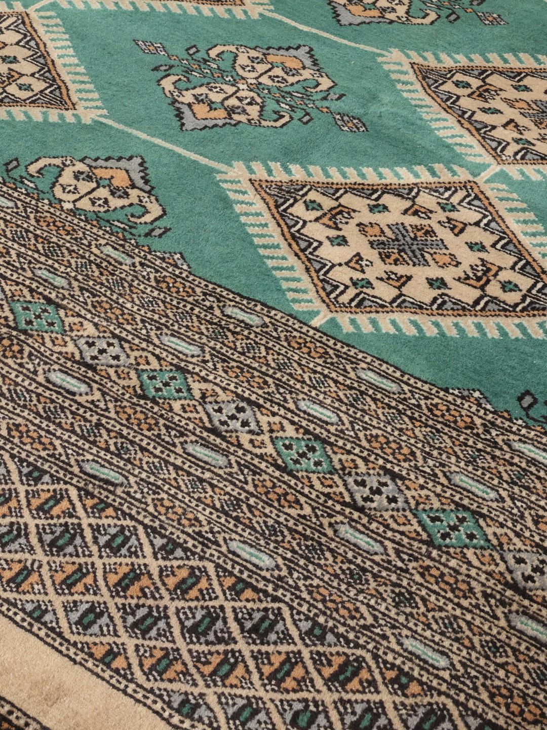 A hand-knotted Pakistan Bokhara rug with a vibrant green field and intricate diamond motifs.