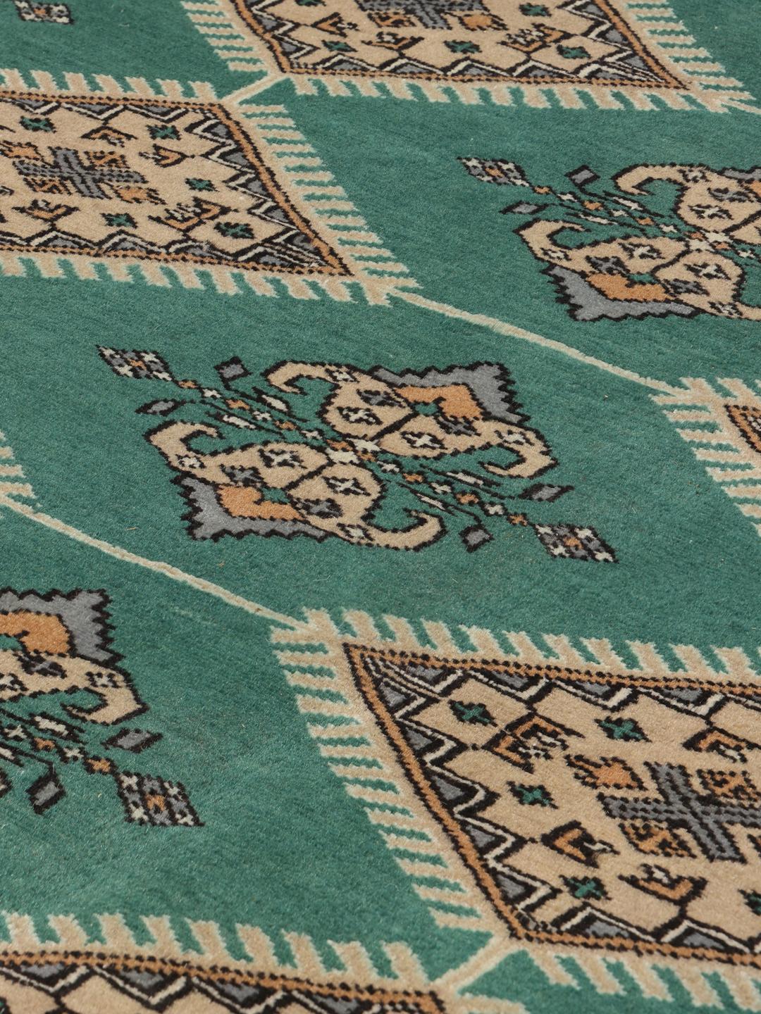 A hand-knotted Pakistan Bokhara rug with a vibrant green field and intricate diamond motifs.