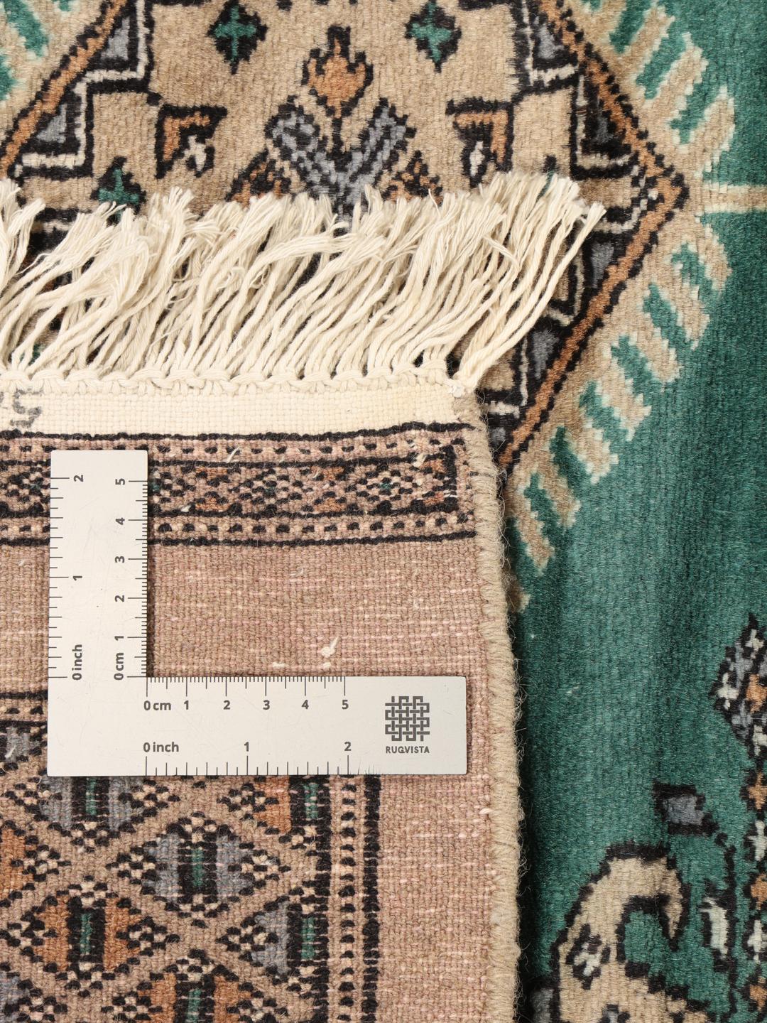 A hand-knotted Pakistan Bokhara rug with a vibrant green field and intricate diamond motifs.