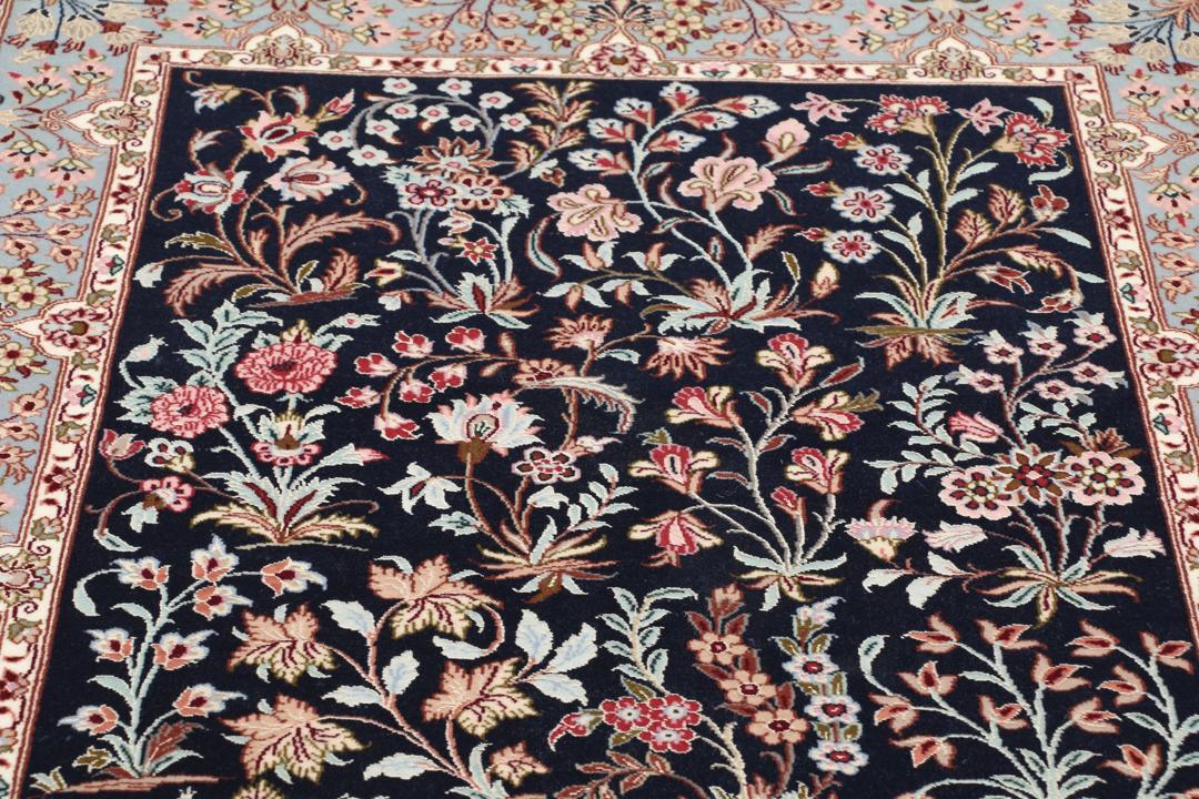 Een met de hand geknoopt Isfahan-tapijt met een ingewikkeld bloempatroon op een donkerblauw veld.