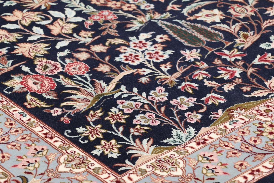 Een met de hand geknoopt Isfahan-tapijt met een ingewikkeld bloempatroon op een donkerblauw veld.
