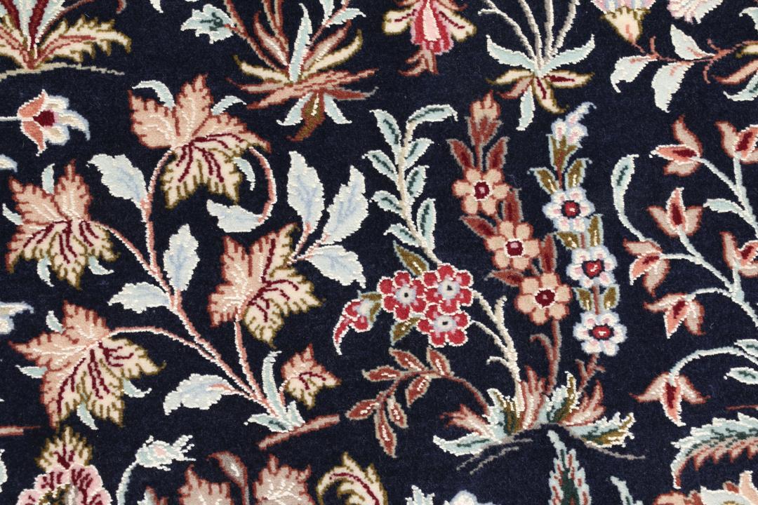 Een met de hand geknoopt Isfahan-tapijt met een ingewikkeld bloempatroon op een donkerblauw veld.