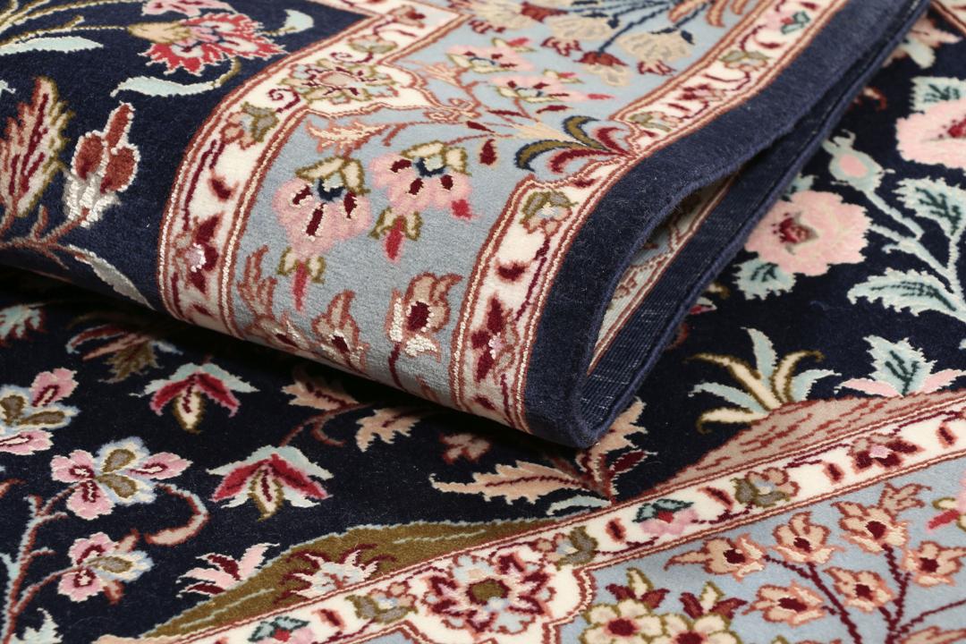 Een met de hand geknoopt Isfahan-tapijt met een ingewikkeld bloempatroon op een donkerblauw veld.