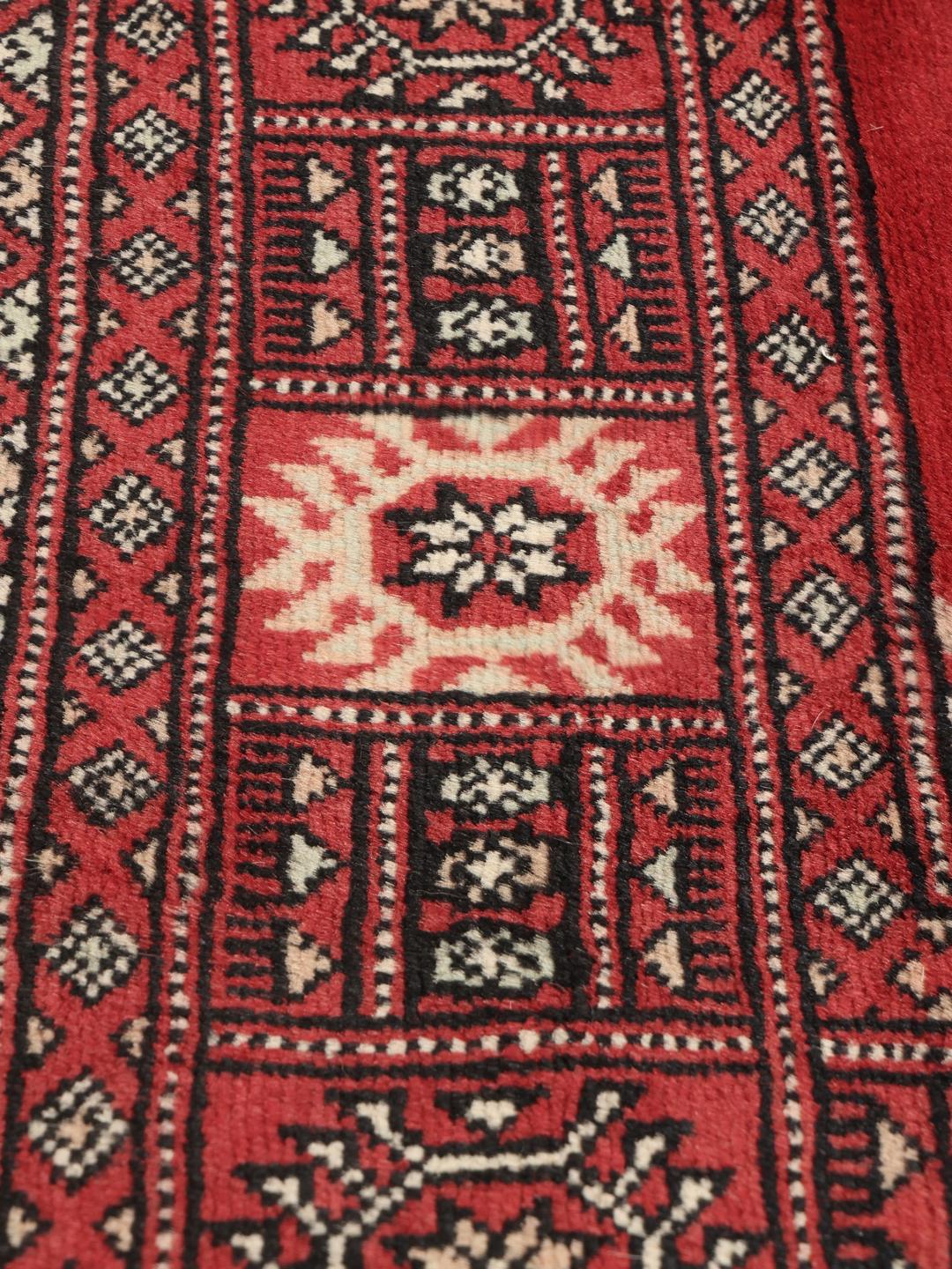 Hand-knotted Pakistan Bokhara rug with a deep red field and traditional motifs.