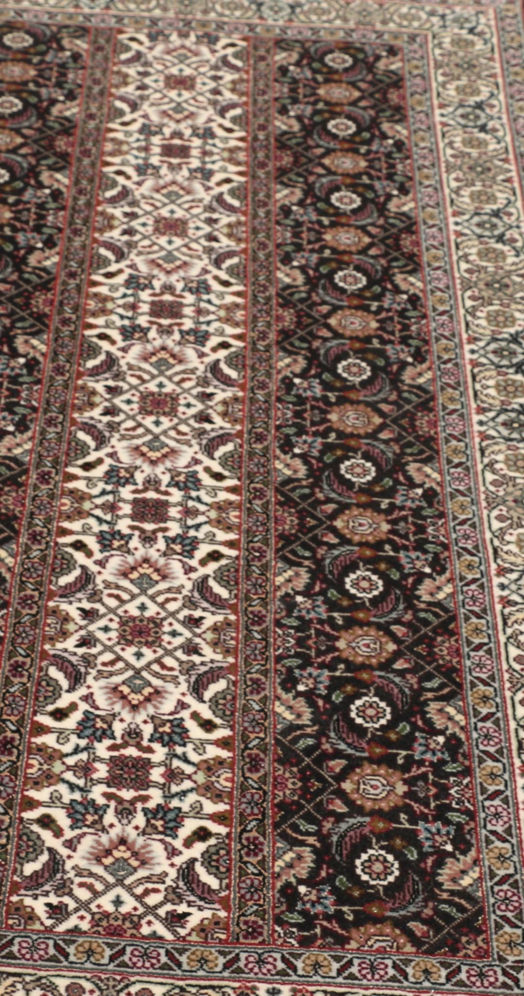 Et rektangulært Tabriz-tæppe fra Mellemøsten med et mørkt, flerfarvet blomsterdesign.