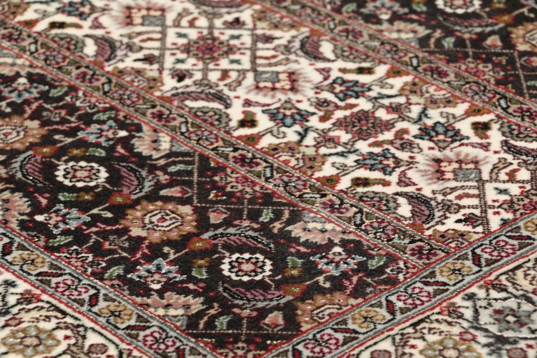 Et rektangulært Tabriz-tæppe fra Mellemøsten med et mørkt, flerfarvet blomsterdesign.