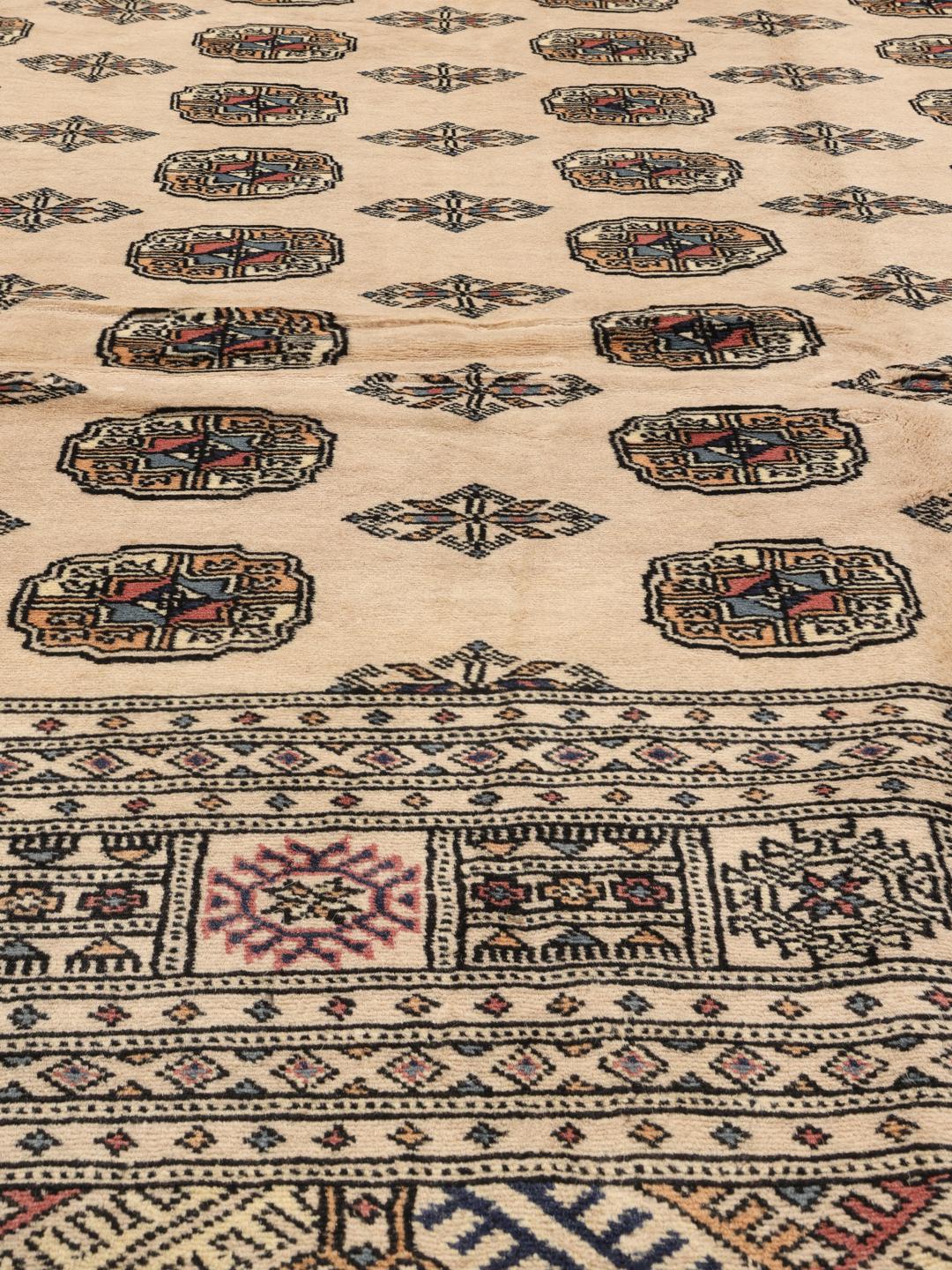 A hand-knotted Pakistan Bokhara 2ply rug with a beige field and traditional repeating motifs.