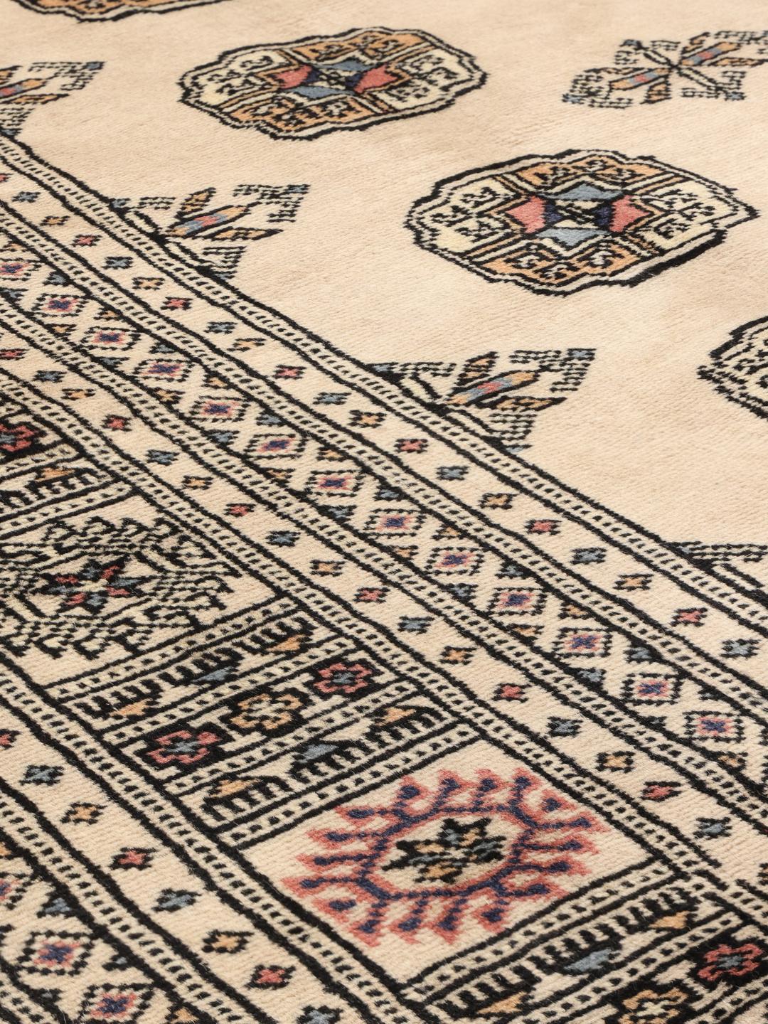 A hand-knotted Pakistan Bokhara 2ply rug with a beige field and traditional repeating motifs.
