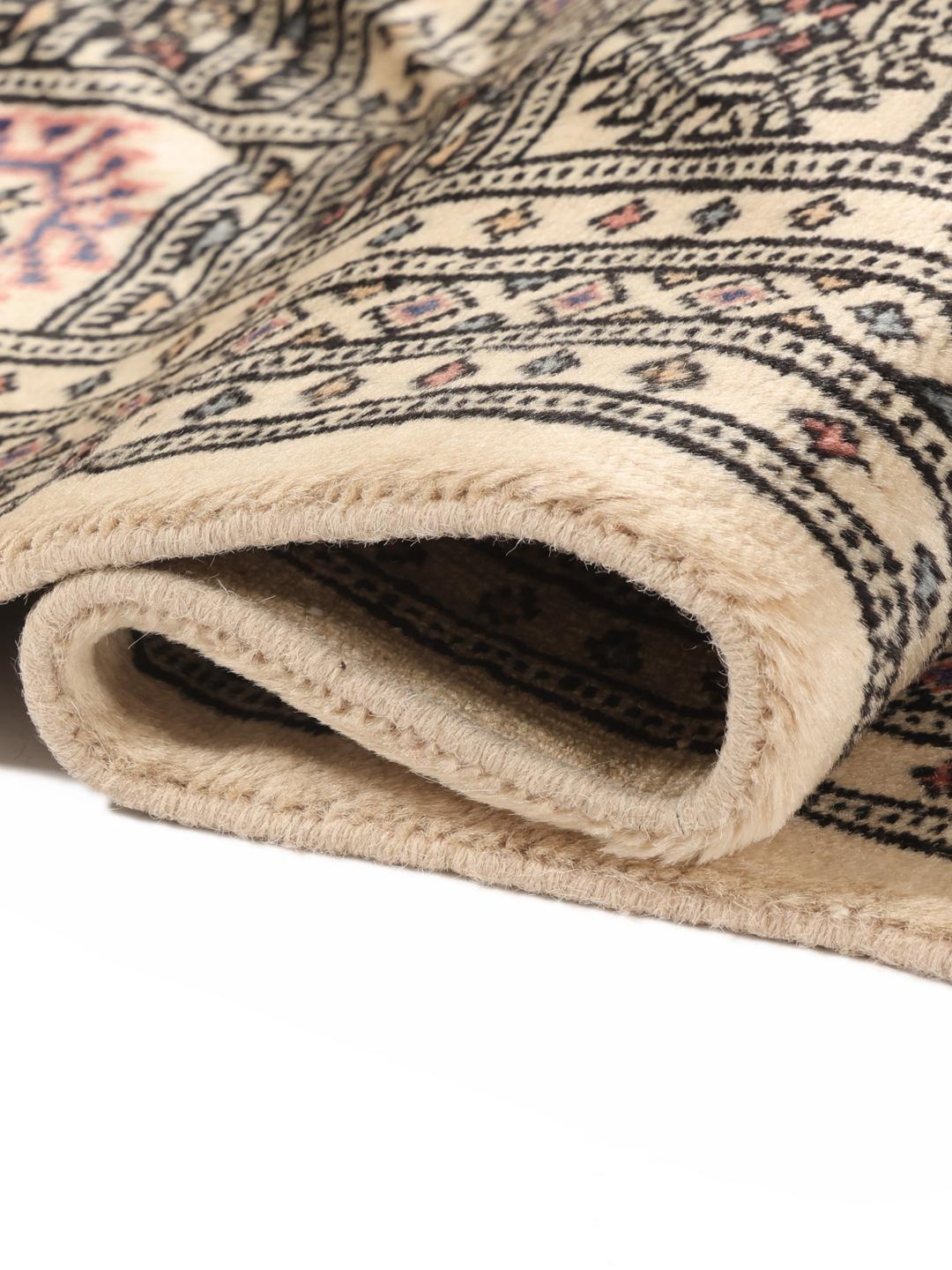 A hand-knotted Pakistan Bokhara 2ply rug with a beige field and traditional repeating motifs.