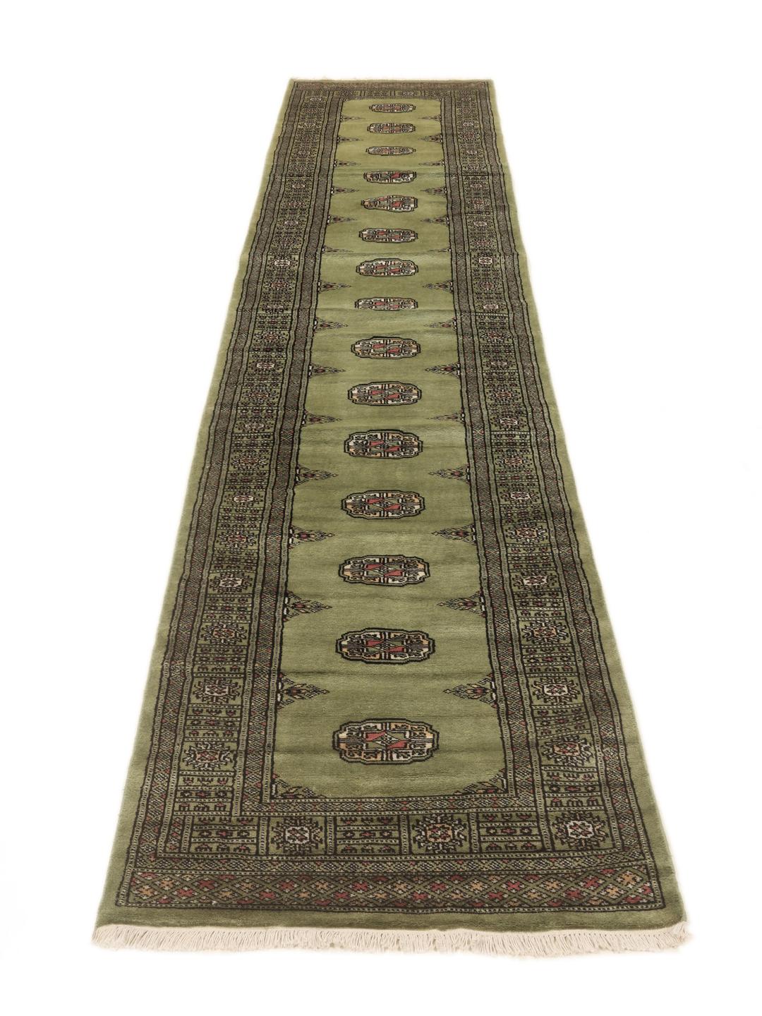 A long, narrow hand-knotted runner from Pakistan with a green field and traditional motifs.