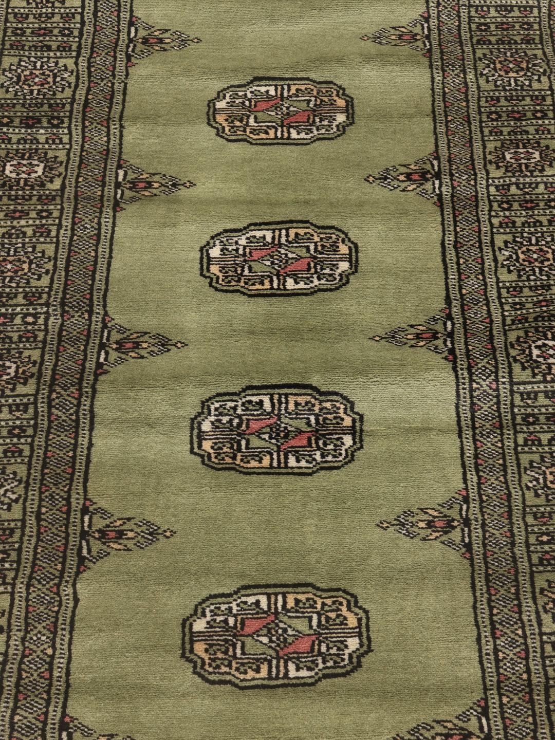 A long, narrow hand-knotted runner from Pakistan with a green field and traditional motifs.