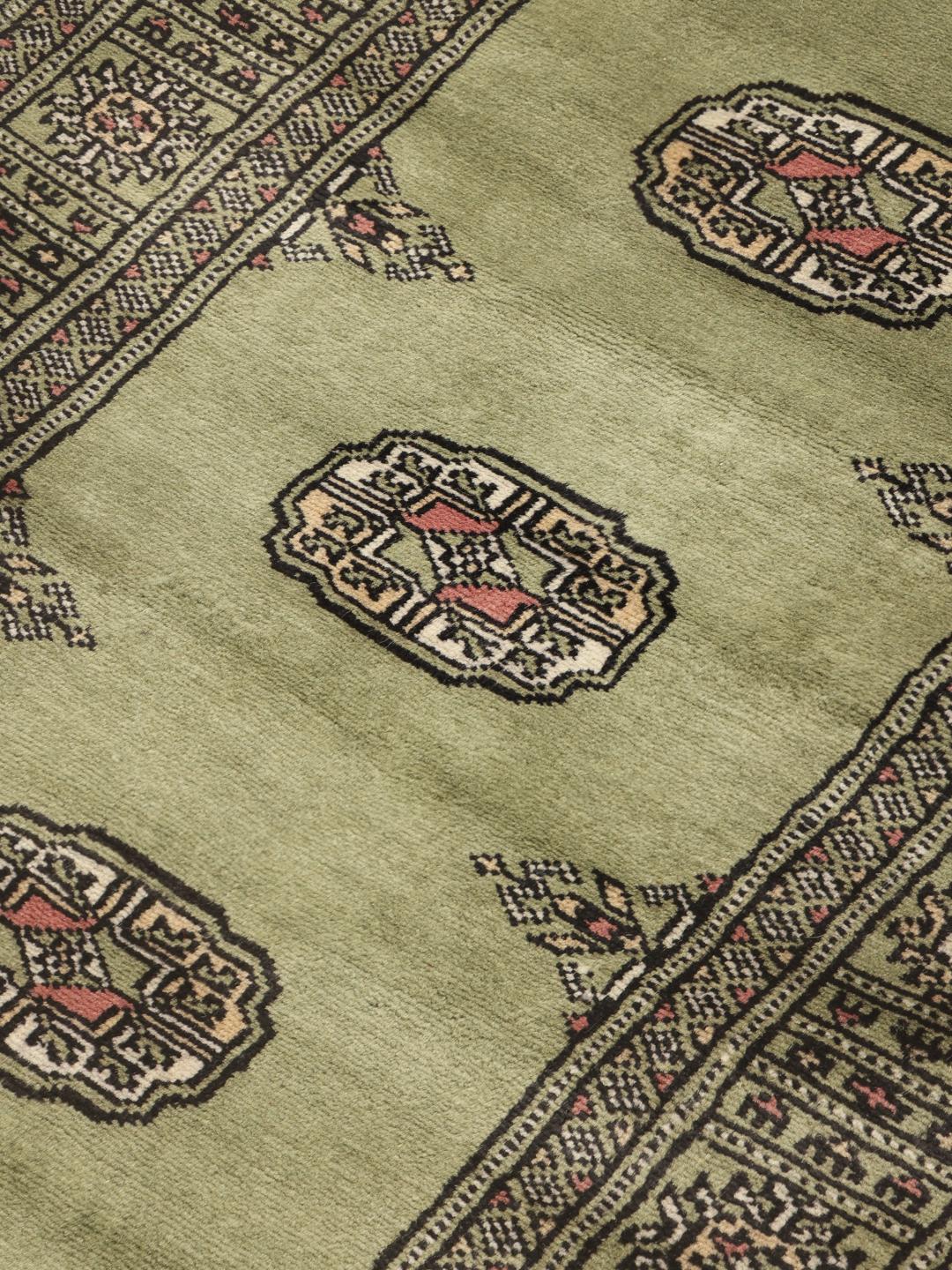 A long, narrow hand-knotted runner from Pakistan with a green field and traditional motifs.