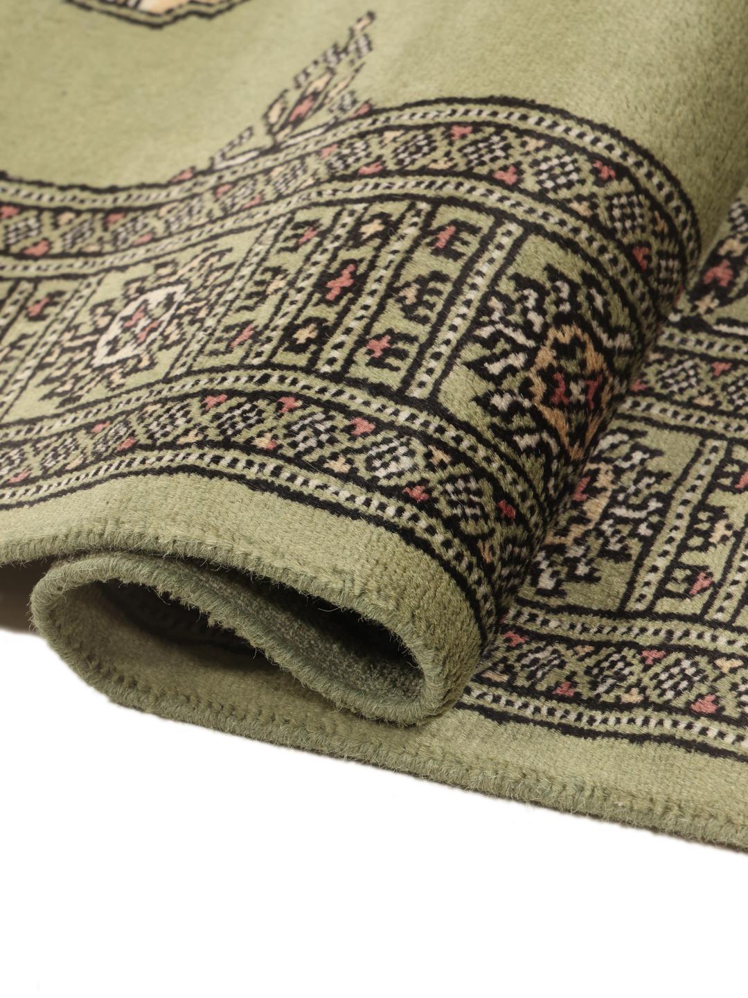 A long, narrow hand-knotted runner from Pakistan with a green field and traditional motifs.