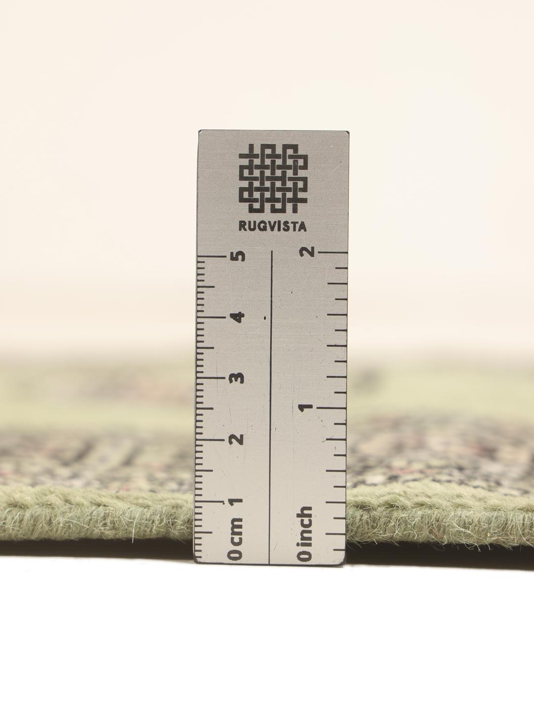 A long, narrow hand-knotted runner from Pakistan with a green field and traditional motifs.